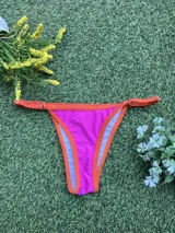 Bikini de dos piezas color fucsia con bordes en naranja. El corpiño es triangular con tirantes finos y la bombacha es colaless regulable con tiras finas laterales.