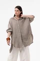 Camisa de lino color beige, de calce amplio y relajado, con cuello camisero, cierre frontal de botones, mangas largas y diseño de largo irregular con aberturas laterales.