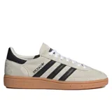 Championes Adidas modelo Handball Spezial, confeccionados en gamuza color beige con las icónicas tres tiras laterales en negro. Presentan suela de goma color caramelo y detalle de talón en negro.
