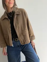 Chaqueta de corte recto color camel, con cierre frontal de cremallera, cuello camisero y puños en tejido de pana a tono. Presenta bolsillos frontales tipo parche y diseño estructurado.