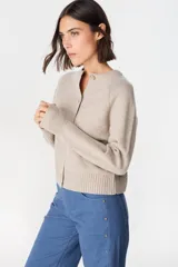 Saco tipo cardigan de punto color crudo, con cuello redondo, cierre frontal de botones y mangas largas con puños acanalados.