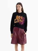 Sweater negro de tejido cálido con cuello redondo y mangas largas. Presenta un bordado frontal multicolor con motivos de fuego y flores.