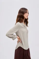 Blusa de viscosa color beige con cuello en V, cierre parcial de botones frontales, bolsillo en el pecho y mangas 3/4.