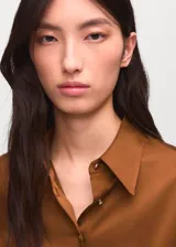 Camisa de corte recto con acabado satinado, cuello camisero clásico, cierre frontal con botones y mangas largas con puños abotonados.