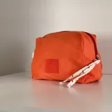 Neceser de tela color coral con cierre superior y detalle de etiqueta de cuero con logo de la marca.