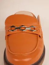 Mocasín tipo mule (abierto en el talón) de símil cuero negro, con suela de plataforma gruesa y taco bajo. Presenta un detalle de cadena metálica dorada sobre el empeine.