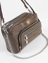 Bandolera negra de cuero vegano con correa ajustable y cadena lateral removible. Presenta un bolsillo frontal con doble cierre horizontal y un logo metálico cuadrado en la parte superior central.