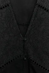 Top negro de escote en V con mangas cortas abullonadas. Presenta detalles de bordados florales a tono y cierre frontal con botones pequeños.