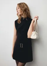 Vestido corto de cuello alto y sin mangas, confeccionado en tejido fluido. Presenta un diseño entallado con cinturón decorativo a la cintura y cierre de cremallera en la parte posterior.