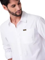 Camisa de manga larga blanca de popelina de algodón, de corte clásico con cuello camisero, cierre frontal con botones y bolsillo en el pecho con etiqueta de la marca.