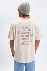 Remera de corte oversize color beige, con estampa en la espalda que incluye nombres y dibujos lineales de personajes de Star Wars.