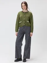 Cardigan de algodón grueso en color rojo, con cuello redondo y cierre frontal de botones grandes. Presenta bolsillos cuadrados en el bajo con detalles de pelo sintético en los bordes y logo bordado en uno de ellos. Posee puños y ruedo elastizados con diseño holgado.