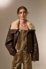 Chaqueta de cuero sintético color marrón, con cuello de piel sintética en tono crema, cierre frontal y diseño holgado.