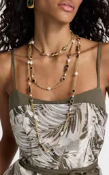 Collar largo de estilo sofisticado con cadena de metal en acabado dorado. Presenta un diseño intercalado con perlas sintéticas y detalles geométricos cuadrados con piedras en tonos rojizos y marrones.