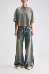 Remera cropped blanca de calce relajado, con cuello redondo, hombros caídos y mangas cortas. Presenta un pequeño detalle de etiqueta bordada en el lateral inferior.