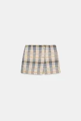 Falda pantalón de tiro alto confeccionada en tejido de tweed con estampado a cuadros en tonos beige, azul y negro. Presenta detalles de falsos botones y cierre lateral con cremallera oculta.