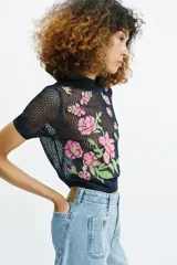 Top de punto calado color azul marino, con cuello subido y manga corta. Presenta un diseño con flores bordadas en tonos rosados y verdes en la parte delantera.