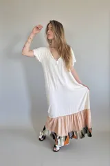 Vestido largo de manga corta con cuello en V, de color crema liso en la parte superior. La falda es de corte amplio con un volante en color melocotón liso, y un volante inferior con estampado abstracto en tonos verde oliva, negro, naranja y azul claro.