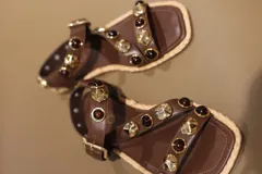 Sandalias bajas negras con tiras de cuero sintético, tachas plateadas y piedras rojas. Suela plana con borde de yute y cierre con hebilla.