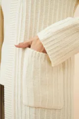 Saco largo tejido en lana color marrón claro con rayas verticales en crudo, con bolsillos laterales y solapas anchas.