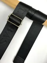 Correa ajustable para cartera confeccionada en cinta tejida con diseño de rayas en negro, blanco y beige, con punteras de cuero sintético negro y herrajes metálicos.