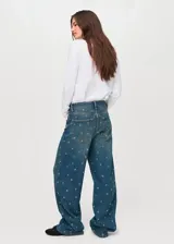 Jeans de tiro medio y corte barrel con diseño de ojales metálicos distribuidos por toda la prenda. Cuenta con cinco bolsillos, cierre de botón y cremallera, y trabillas para cinturón.