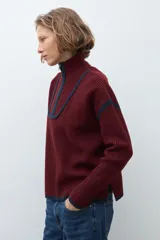 Sweater de punto color crudo con cuello alto y cierre frontal parcial. Presenta detalles de vivos en color marrón en el cuello, hombros y ruedo, con diseño de manga larga.