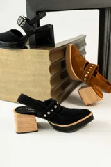 Zapatos tipo zueco de gamuza negra con punta fina y tira sobre el empeine decorada con tachas metálicas plateadas. Posee taco cuadrado de madera y suela con plataforma.