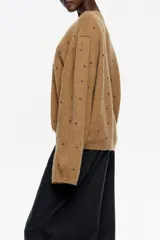 Sweater de punto en color gris oscuro, con corte boxy y escote en caja. Presenta mangas largas rectas y está decorado con pequeños remaches plateados distribuidos por toda la prenda. Confeccionado en una mezcla de lana y alpaca que aporta calidez.