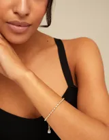 Pulsera de cadena compuesta por pequeños eslabones ovalados de acabado brillante, con cierre de mosquetón y dije colgante pequeño.