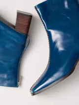 Bota de caña media en cuero negro con punta cuadrada y taco de madera. Cuenta con una costura bordada en color contrastante en el empeine y cierre en la parte trasera.