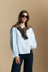 Camisa de manga larga color celeste, con cuello clásico, cierre frontal con botones y puños elastizados con volados. Presenta un diseño fluido con detalle de vainilla en la espalda.