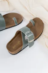 Sandalias planas de cuero color verde seco, con diseño cruzado, hebilla metálica regulable y tira al dedo.