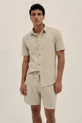 Camisa de manga corta en tejido ligero de lino y algodón a rayas verticales en tonos beige y blanco. Tiene botones de madera y un parche con el logo de la marca.