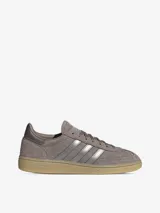 Championes Adidas modelo Handball Spezial de perfil bajo, confeccionados en gamuza color marrón topo con las clásicas tres tiras y detalles metalizados en tono plateado, inscripción lateral en relieve y suela de caucho translúcido.