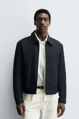 Cazadora cropped fit color azul marino, confeccionada en tejido de algodón. Presenta cuello solapa, manga larga con puño abotonado, bolsillos frontales de vivo y un bolsillo interior. El cierre es frontal con cremallera.