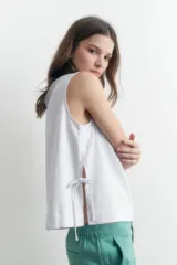 Blusa blanca sin mangas confeccionada en lino, con corte recto y aberturas laterales ajustables con lazos.