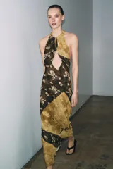 Vestido largo de viscosa con estampado floral y diseño de paneles diagonales en tonos tierra. Presenta cuello halter con cierre de botones y abertura frontal en el pecho, dejando los hombros al descubierto.