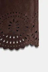 Pantalón culotte marrón de tiro alto con efecto ante, bolsillos delanteros y traseros, pernera ancha y corta. El bajo está troquelado con un diseño floral. Cierre frontal con cremallera y botón.