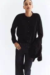 Saco negro de punto suave con lana, corte holgado, hombros caídos, cuello redondo y botones frontales. Remates acanalados en cuello, puños y bajo.