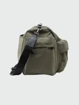 Bolso tipo duffle o bolso de viaje de color verde militar, con múltiples bolsillos exteriores con tapa y correa ajustable de tela negra con detalles en cuero sintético negro.
