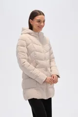 Campera acolchada color beige claro, de largo medio, con capucha y cierre frontal. Presenta costuras horizontales y diagonales que crean un efecto matelassé.