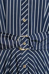 Vestido midi azul marino con rayas blancas, cuello solapa, escote en V y cierre frontal con botones. Cuenta con mangas abullonadas por debajo del codo con puños anchos a contraste, cinturón ajustable del mismo tejido con hebilla metálica y falda evasé.