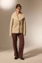 Chaqueta de eco-cuero color beige con interior y cuello de piel sintética al tono. Presenta un diseño holgado, cierre frontal con un botón y solapas amplias.
