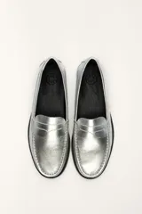 Mocasín de cuero vacuno color plateado, con costuras visibles en el empeine y suela de cuero negra.