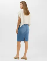 Falda de denim en lavado azul medio con efecto de desgaste localizado, de silueta tubo y largo a la rodilla. Presenta tiro medio-alto, pretina con trabillas, cierre frontal con cremallera y botón metálico, bolsillos frontales y costuras verticales que estructuran la prenda.