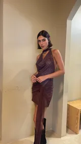 Vestido corto de microtul color marrón, con escote tipo buche y cuello halter. Presenta un diseño con superposición de tela en la falda que crea un efecto drapeado con un lazo lateral largo.