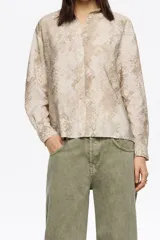 Camisa de corte boxy con cuello camisero, cierre frontal de botones y mangas largas con puños abotonados. Presenta un estampado animal print en tonos neutros.