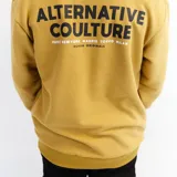 Buzo mostaza de algodón extra suave con cuello redondo y puños y cintura acanalados. Estampado en la espalda con la frase "Alternative Culture" y nombres de ciudades.