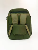 Mochila de color verde oliva con paneles en tonos de verde contrastantes y detalles en negro. Presenta un bolsillo frontal con cierre y un pequeño parche rectangular con texto en la parte inferior.